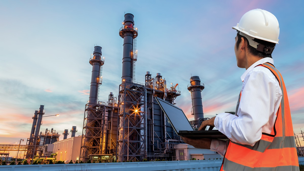 homem com computador observa uma refinaria de óleo e gás