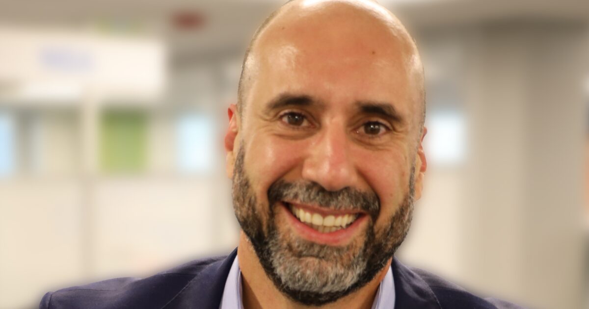 Spencer Gracias, diretor geral da Kyndryl Brasil, sorrindo em um ambiente corporativo com fundo desfocado. A imagem transmite um semblante amigável e confiante, destacando sua posição de liderança (especializado em combater ciberataque)