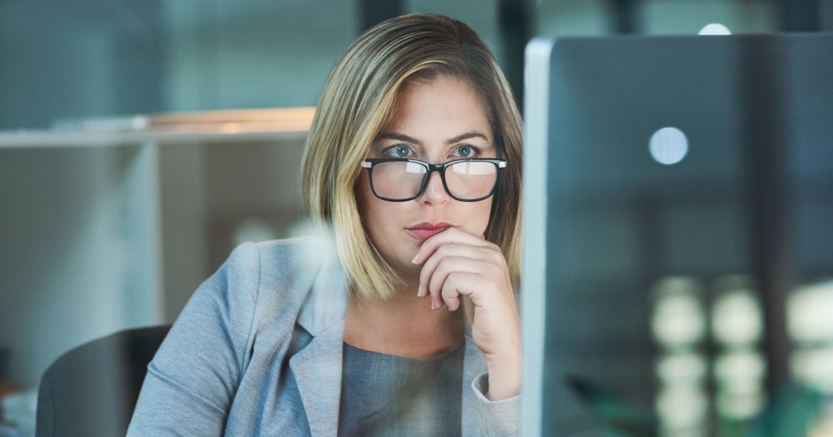 Mulher executiva de óculos, com expressão concentrada, analisando informações em uma tela de computador. Ela está em um ambiente de escritório moderno, vestindo um blazer cinza, transmitindo foco e profissionalismo (pensamento computacional, profissionais de TI, executiva, trabalho, mulher, trabalhadora, trabalhadores, profissionais, cresce)