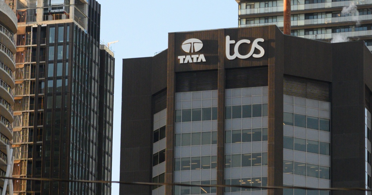 Fachada de um edifício corporativo com os logotipos da Tata Consultancy Services (TCS) e Tata no topo. O prédio está localizado em um ambiente urbano, cercado por outros edifícios modernos em construção ou finalizados (tcs, Tata Consultancy Services, nvidia)