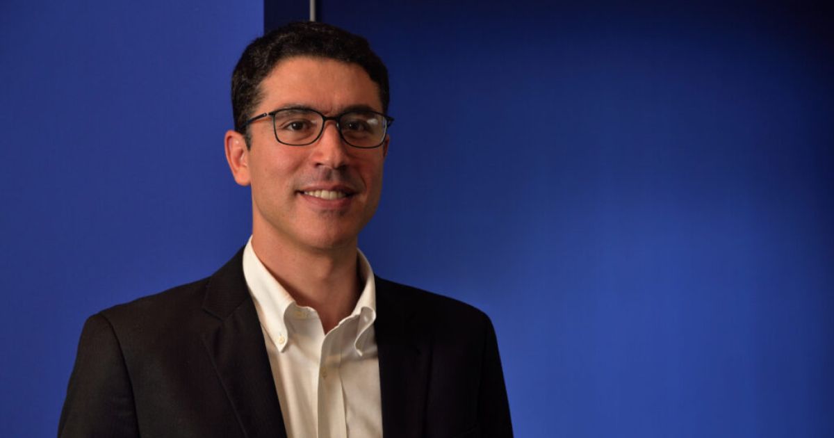 Imagem de Marcelo Mearim, CEO da Sofya no Brasil, posando com um sorriso. Ele usa óculos, veste um terno escuro e camisa branca, com um fundo azul sólido que transmite profissionalismo e seriedade Marcelo Mearim, Sofya