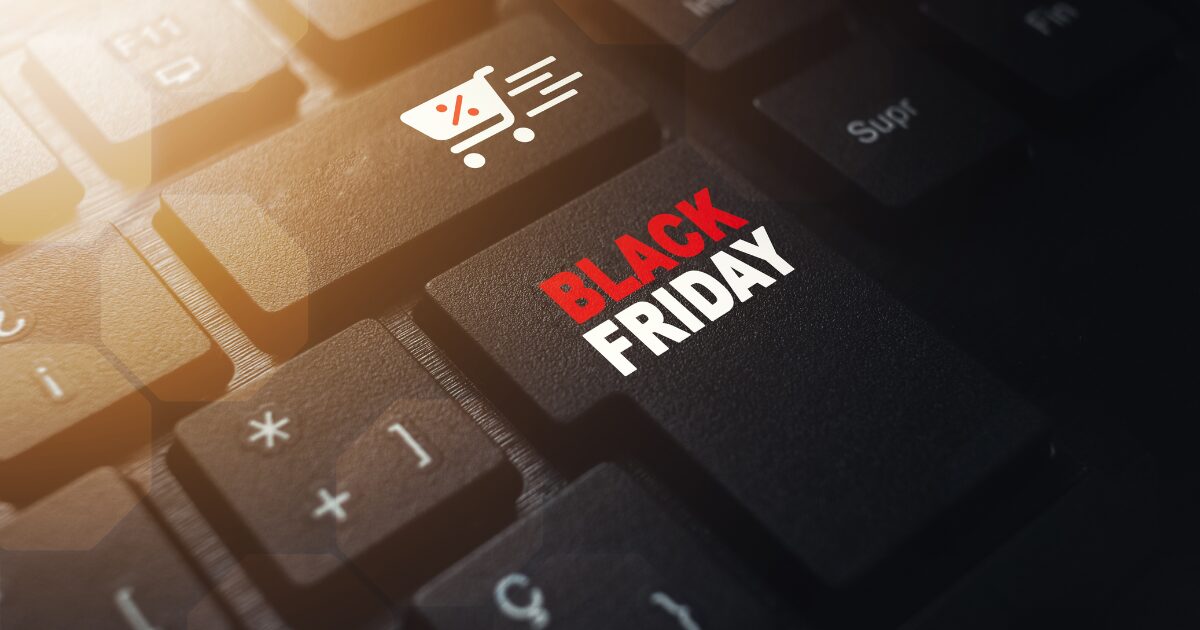 Imagem de um teclado de computador com destaque para uma tecla personalizada que exibe o texto 'Black Friday' em letras brancas e vermelhas, ao lado de um ícone de carrinho de compras com um símbolo de desconto. A iluminação cria um efeito de destaque, simbolizando compras online e promoções da Black Friday