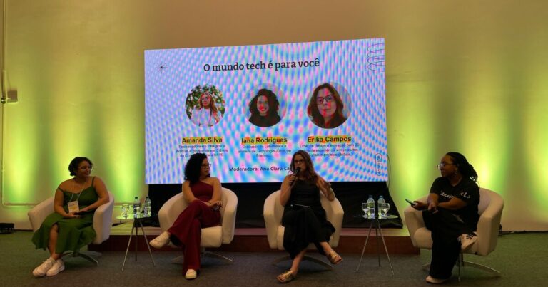 Mulheres participam de um painel em um evento sobre tecnologia, com o tema "O mundo tech é para você". Na tela ao fundo, aparecem os nomes e perfis das palestrantes: Amanda Silva, pesquisadora em inteligência artificial; Iana Rodrigues, analista de tecnologia; e Erika Campos, líder de design e inovação. A moderadora, Ana Clara Camêlo, também está presente na discussão. As quatro mulheres estão sentadas em cadeiras brancas e envolvidas na conversa, abordando temas de inclusão e oportunidades para mulheres na área de tecnologia.