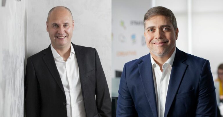 A imagem mostra dois executivos da empresa Objective. À esquerda, João Paulo Miranda, CEO da Objective, aparece sorrindo e com um traje formal, utilizando um blazer preto e camisa branca. À direita, Jorge Sellmer, CRO da Objective, também sorri, vestindo um terno azul e camisa branca. O ambiente de fundo é moderno, com elementos que sugerem um escritório corporativo. Ambos estão posicionados de forma que destacam a personalidade de cada um, com um clima profissional e acolhedor.