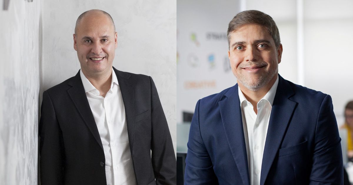 A imagem mostra dois executivos da empresa Objective. À esquerda, João Paulo Miranda, CEO da Objective, aparece sorrindo e com um traje formal, utilizando um blazer preto e camisa branca. À direita, Jorge Sellmer, CRO da Objective, também sorri, vestindo um terno azul e camisa branca. O ambiente de fundo é moderno, com elementos que sugerem um escritório corporativo. Ambos estão posicionados de forma que destacam a personalidade de cada um, com um clima profissional e acolhedor.