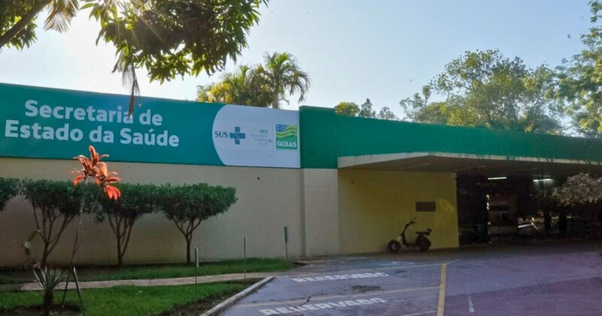 Fachada da Secretaria de Estado da Saúde de Goiás, com uma placa verde exibindo o logotipo do SUS e a identificação do órgão. O local é cercado por árvores e vegetação, com um ambiente ensolarado que destaca a entrada do prédio (orgãos, goiás, secretaria de saúde, Imagem SES-GO Divulgação)