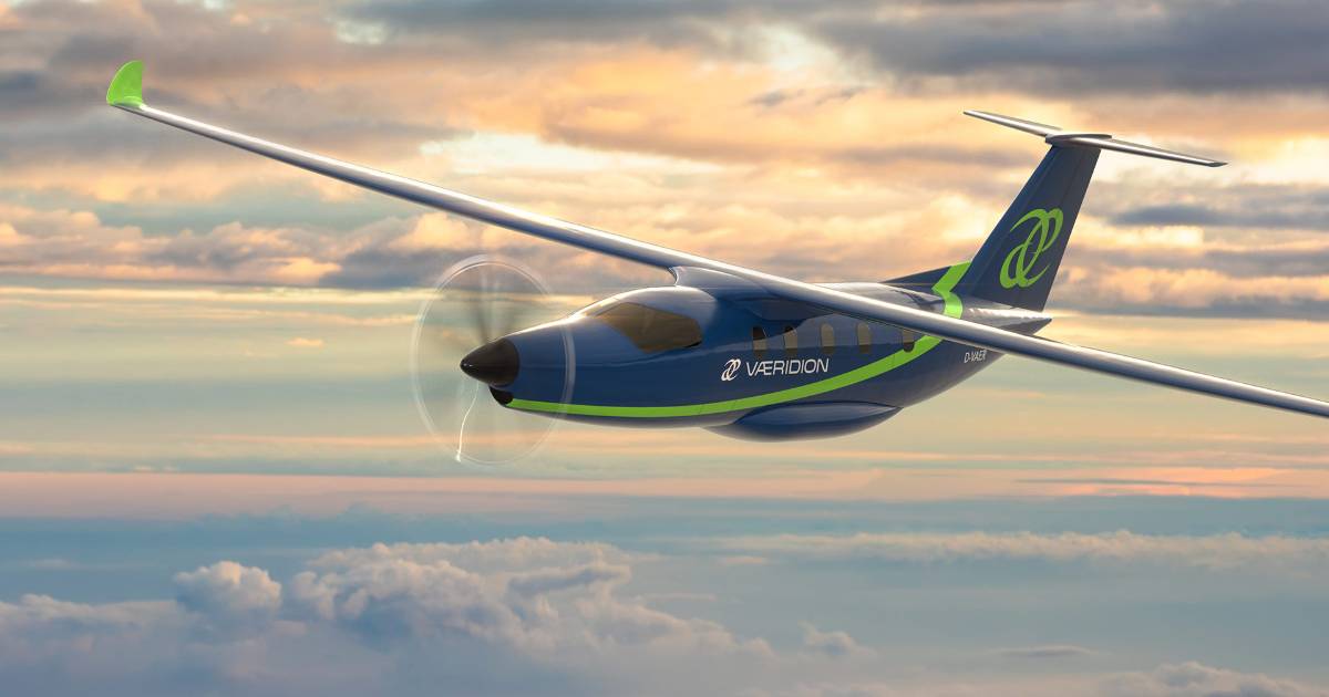A imagem mostra um avião futurista em voo, com um design moderno e aerodinâmico. O avião, identificado com a marca "Vaeridion", é de cor predominante azul com detalhes em verde, e está voando acima das nuvens em um céu com tons de laranja e azul. O modelo possui asas longas e uma hélice na frente. O cenário transmite uma sensação de inovação tecnológica e sustentabilidade no setor da aviação, voos elétricos