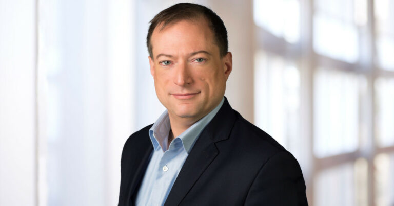 John Roese, Chief Technology Officer (CTO) e Chief AI Officer (CAIO) global da Dell Technologies, em uma foto profissional. Ele veste um terno escuro com camisa azul clara, posando com expressão confiante e fundo desfocado de ambiente corporativo