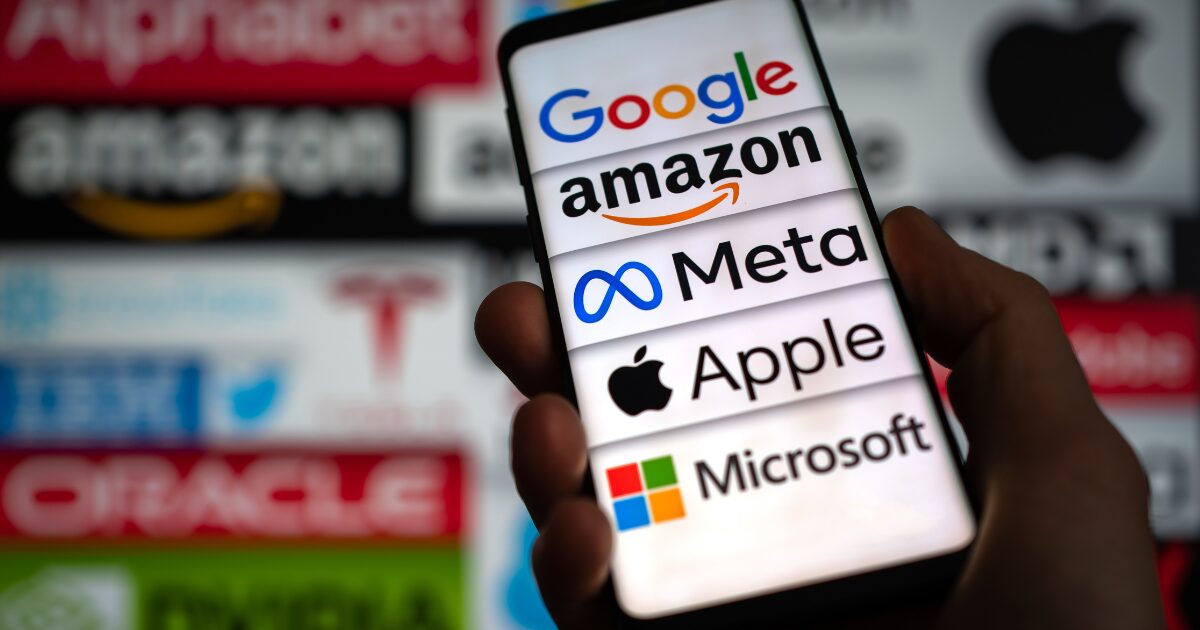 Imagem de um smartphone exibindo os logotipos de grandes empresas de tecnologia, como Google, Amazon, Meta, Apple e Microsoft, em destaque na tela. Ao fundo, desfocado, estão os logos. (big techs) Nasdaq, antitruste