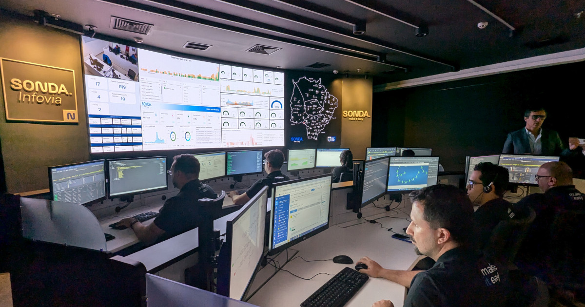 Imagem do novo Centro de Operações Integradas (COI) da Sonda no Brasil. A sala apresenta uma equipe de profissionais monitorando diversos sistemas em múltiplos monitores. No fundo, grandes painéis exibem gráficos, mapas e indicadores de desempenho. O ambiente é moderno e tecnológico, com iluminação focada