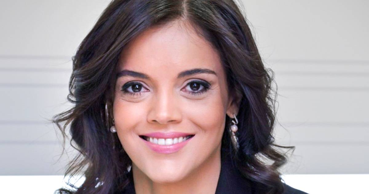 Retrato de Ana Paula Assis, nova vice-presidente sênior da IBM para a região EMEA (Europa, Oriente Médio e África). Na imagem, ela aparece sorridente, com cabelos castanhos ondulados, usando brincos de pérola e vestindo traje formal, transmitindo uma postura profissional e acolhedora. O fundo é claro e neutro, destacando o foco na executiva