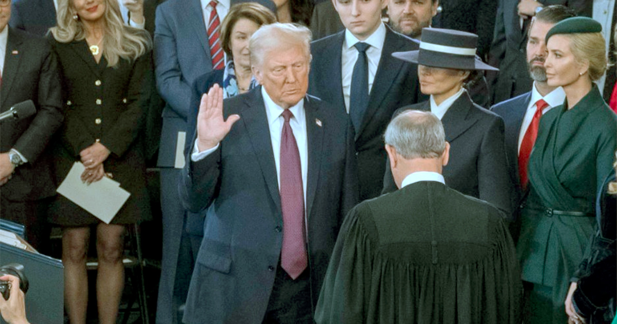 Imagem de Donald Trump durante sua cerimônia de posse como presidente dos Estados Unidos, levantando a mão direita enquanto faz o juramento oficial. Ele está rodeado por familiares, autoridades e convidados, incluindo Melania Trump ao seu lado, com um traje formal e chapéu, em um ambiente solene (trolls, dei)