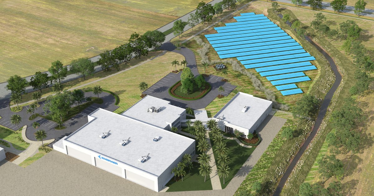 Vista aérea de instalações da Embraer em Melbourne, Flórida, cercadas por áreas verdes. Ao lado dos edifícios, há um grande campo de painéis solares azuis, destacando o uso de energia renovável. A imagem demonstra integração entre tecnologia, sustentabilidade e infraestrutura moderna