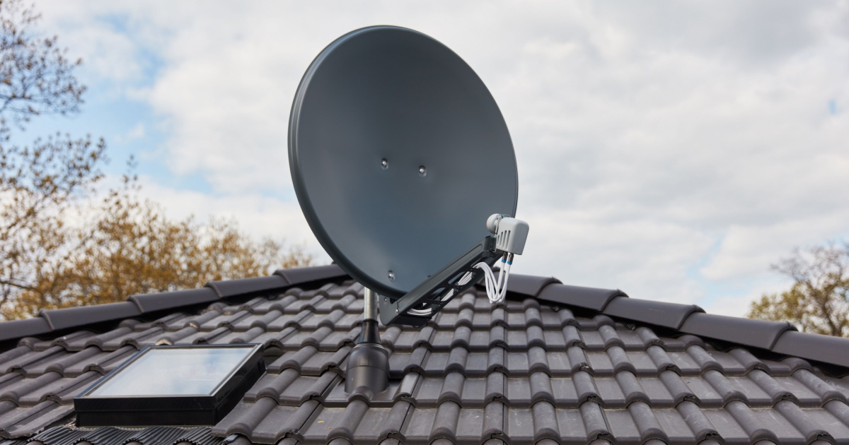 Imagem de uma antena parabólica instalada no telhado de uma casa com telhas escuras, céu parcialmente nublado ao fundo, representando tecnologia de comunicação via satélite (antena parabolica, 3,5GHz, automatização, automatiza)