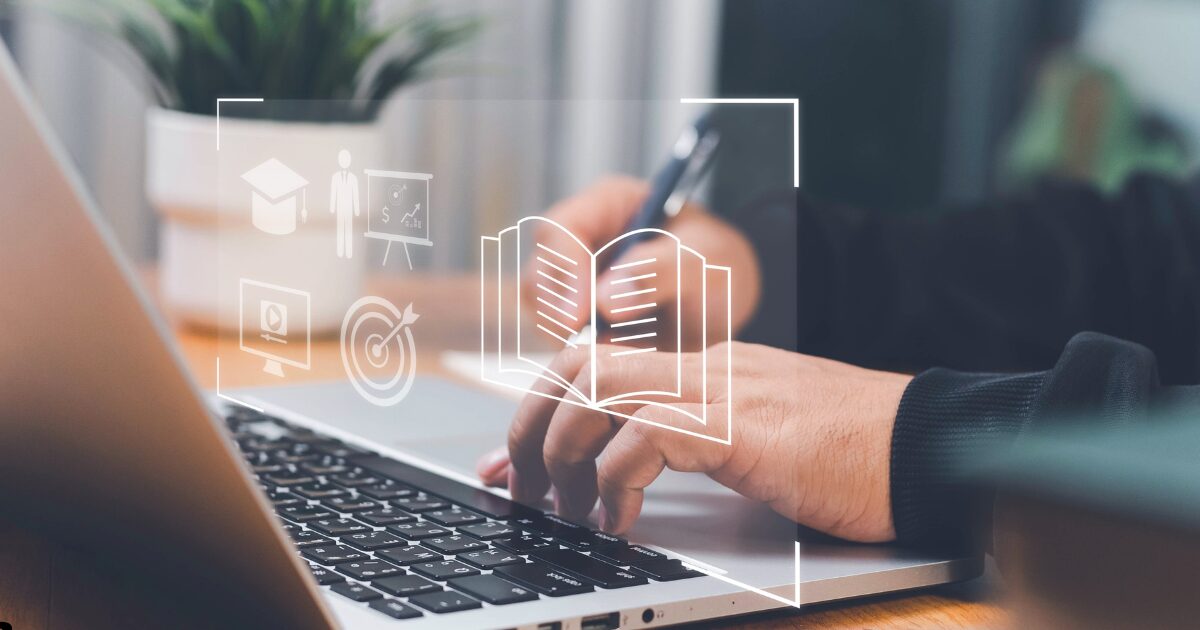 Uma pessoa utilizando um notebook, segurando uma caneta na mão direita e digitando com a esquerda. Sobreposta à imagem estão ícones representativos de educação online, como livro aberto, alvo, apresentação em vídeo, pessoa apresentando gráfico e um capelo (chapéu de formatura). O fundo é desfocado e inclui uma planta decorativa, transmitindo uma atmosfera profissional e focada em aprendizado digital (tecnologia)