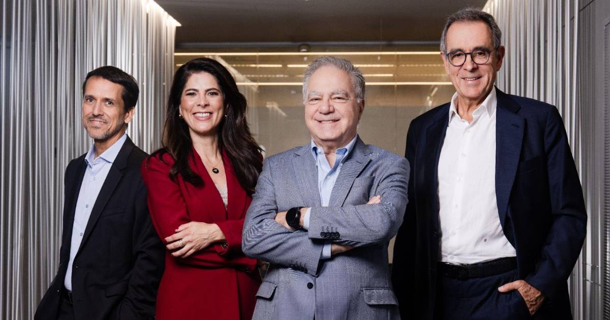Imagem do time de liderança da Claro, posando em um ambiente corporativo com iluminação moderna e fundo com divisórias verticais. Da esquerda para a direita estão: Rodrigo Marques, CEO da Claro, vestindo terno escuro; Roberta Godoi, CEO da Unidade para Pequenas e Médias Empresas, com vestido vermelho e sorrindo; José Félix, presidente, com paletó cinza claro e braços cruzados; e José Formoso, CEO da Unidade de Grandes Empresas e Governo, usando terno escuro e óculos. Todos demonstram postura confiante e profissional