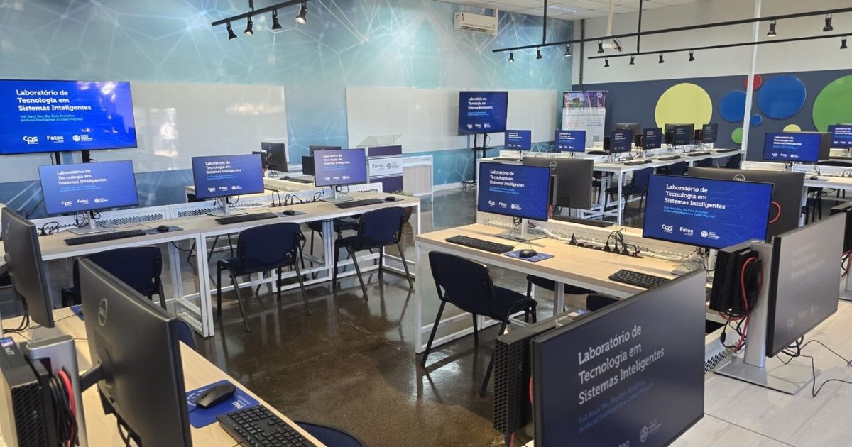 A imagem mostra uma sala moderna e bem equipada da Faculdade de Tecnologia (Fatec) de Pompeia, no interior de São Paulo. Trata-se do Laboratório de Tecnologia em Sistemas Inteligentes, conforme identificado nas telas dos computadores distribuídos pelas bancadas. O ambiente é amplo, iluminado e preparado para atividades práticas em tecnologia da informação e inteligência artificial. Ao fundo, há painéis com design moderno e colorido, além de uma parede com lousas brancas e uma tela grande exibindo o nome do laboratório. As estações de trabalho estão organizadas em fileiras, cada uma equipada com computadores de mesa, teclados, mouses e cadeiras acolchoadas. O ambiente reflete um espaço inovador voltado à formação técnica e aplicada de estudantes da instituição.
