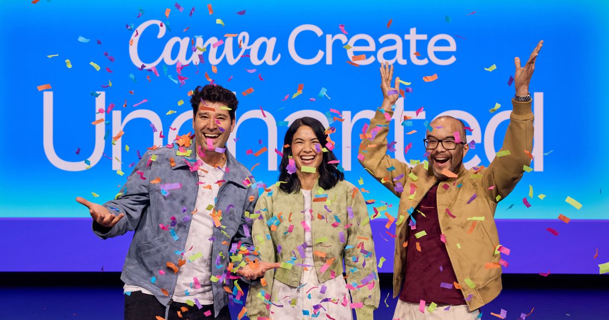 Três pessoas em palco, sorridentes e celebrando debaixo de uma chuva de confetes coloridos. Estão posicionadas em frente a um grande ecrã azul com o texto “Canva Create Uncharted”. O grupo, composto por dois homens e uma mulher, veste roupas casuais e demonstra entusiasmo e alegria, com expressões felizes e braços erguidos.