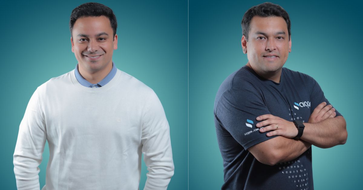Thiago Felippe, CEO da Aiqon (à esquerda), usando suéter branco e camisa azul clara, e Edson Oguma, líder da área de conformidade da Aiqon (à direita), com camiseta escura da empresa e braços cruzados. Fundo azul esverdeado. Foto: Divulgação.