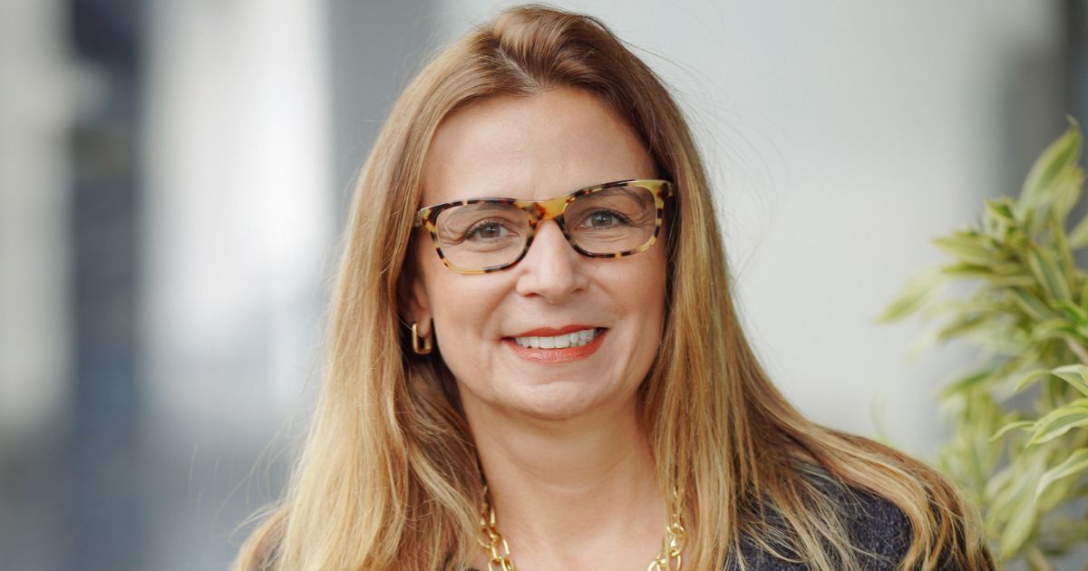 Luciana Pinheiro, diretora-geral da Citrix no Brasil, sorri em retrato profissional. Ela usa óculos de acetato com armação estampada, batom coral e colar dourado. Está com os cabelos soltos, lisos e loiros, vestindo blazer escuro. Ao fundo, o ambiente é corporativo e desfocado. Foto: Divulgação.