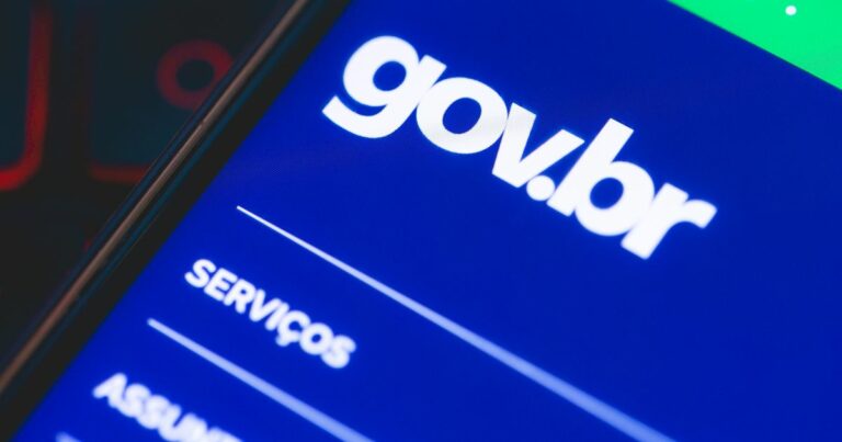Imagem em close-up do ecrã de um smartphone a exibir a interface do portal digital do governo brasileiro, com o logótipo “gov.br” em letras brancas sobre um fundo azul. Abaixo, vê-se parcialmente a palavra “SERVIÇOS”, sugerindo a navegação por opções disponíveis no site. A imagem transmite a ideia de acesso digital a serviços públicos.