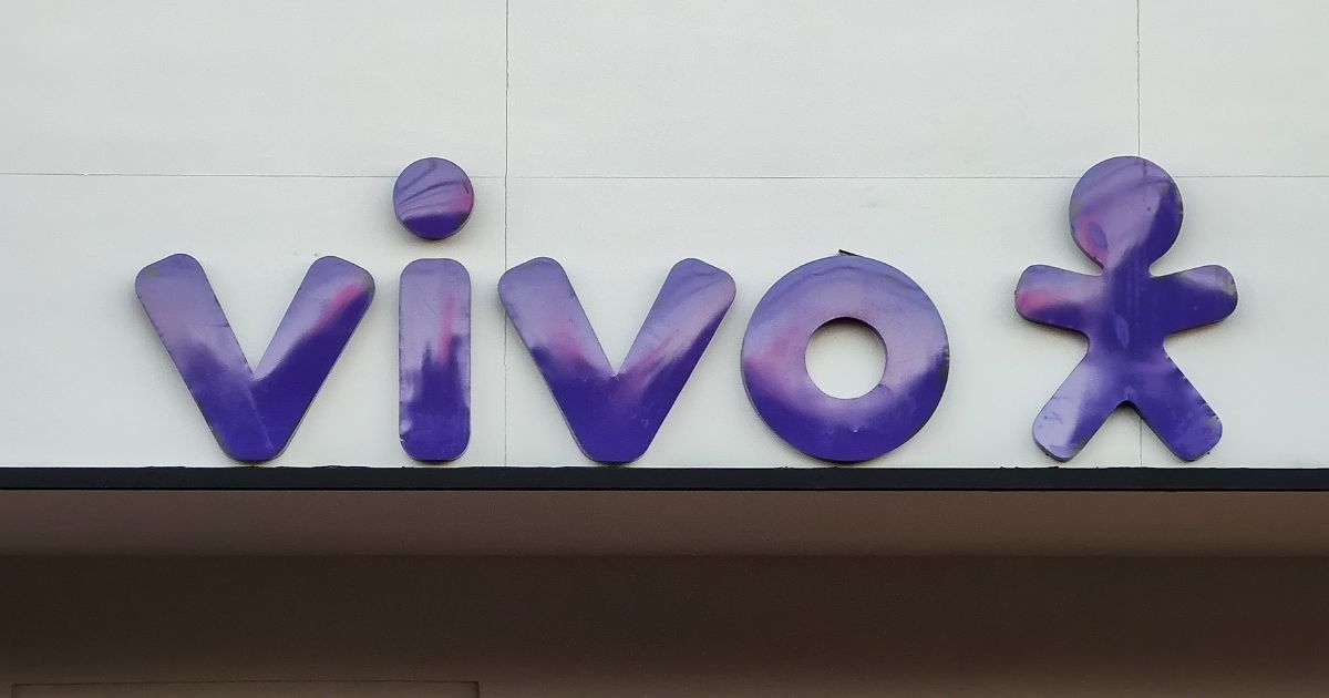 Logótipo da operadora de telecomunicações "Vivo" em letras minúsculas, com tipografia arredondada na cor roxa com reflexos rosados. À direita da palavra, está o símbolo da marca: uma figura humana estilizada com braços e pernas abertas, também em roxo., solução