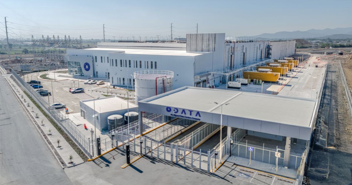 Duas mãos robóticas avançadas, uma à esquerda e outra à direita, estão prestes a se tocar através de um globo digital translúcido flutuante no centro da imagem. O globo mostra continentes como América do Sul, África e Europa, com cores vibrantes que vão do azul ao amarelo e vermelho no centro, criando um efeito de calor ou energia. O fundo é escuro e abstrato, com pontos de luz azulados e linhas conectando nós, sugerindo redes digitais ou conexões de dados. A cena transmite um tema de tecnologia avançada, inteligência artificial e conexão global.