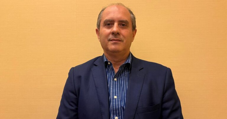 Victor Murad Filho, subsecretário de Transformação do Governo do Espírito Santo, posa em frente a uma parede bege, vestindo blazer azul-marinho e camisa listrada. Foto: Déborah Oliveira.