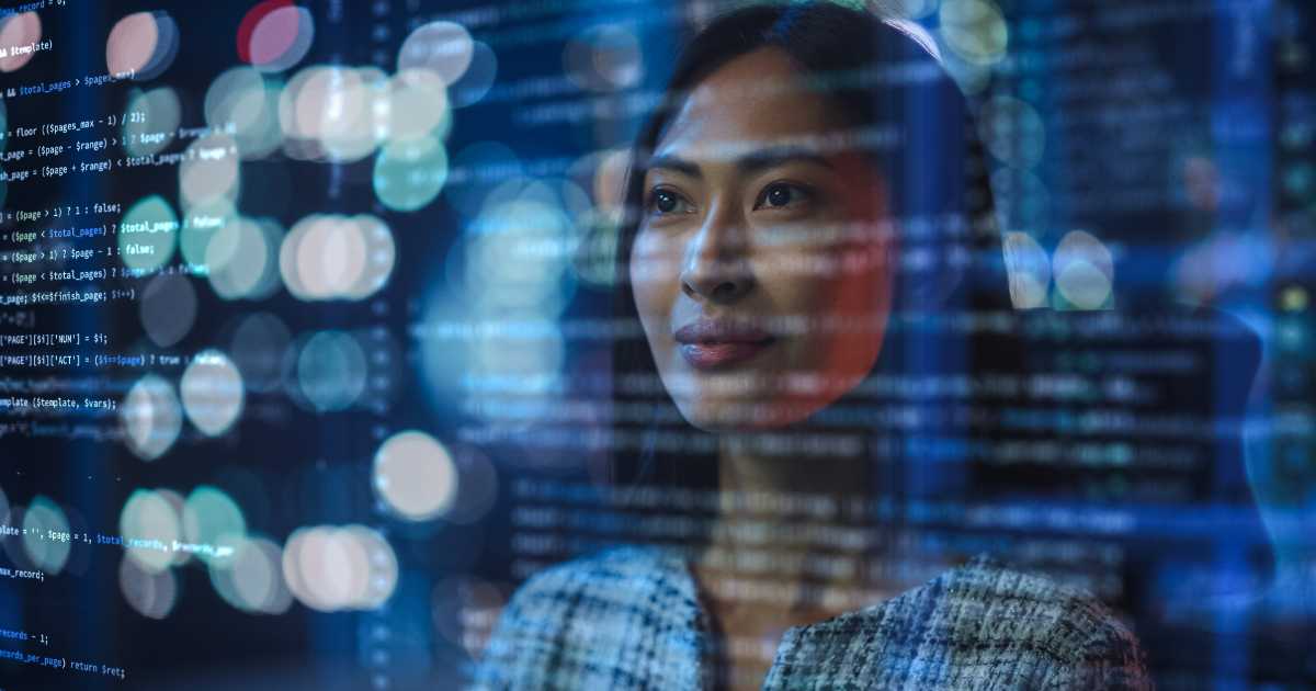 Imagem de uma mulher olhando pensativamente através de uma tela de vidro com códigos de programação projetados sobre ela, simbolizando o uso de inteligência artificial e tecnologia. O fundo apresenta luzes desfocadas, reforçando o ambiente tecnológico e moderno. A expressão da mulher transmite foco e reflexão (pensamento, meta)