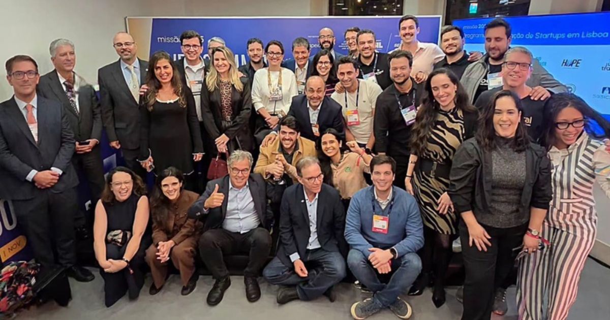 A imagem mostra um grupo grande de pessoas reunidas em um ambiente corporativo ou de evento, provavelmente relacionado a negócios, startups ou tecnologia. O cenário sugere uma foto oficial de grupo durante uma conferência ou missão empresarial. (ApexBrasil)