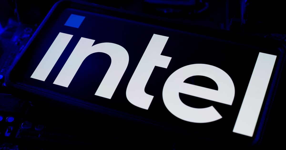 A foto mostra um close-up do logotipo da Intel em destaque. O logotipo está em letras minúsculas brancas sobre um fundo preto, com iluminação azul ao redor, criando um efeito tecnológico e moderno. A imagem transmite uma estética associada à marca de tecnologia, com foco no nome “intel” centralizado e bem visível.