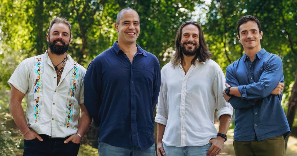 A imagem mostra quatro pessoas em pé, em um ambiente externo com bastante vegetação ao fundo, sugerindo um parque ou área arborizada. A cena parece informal e descontraída. (Diva e Ginga)