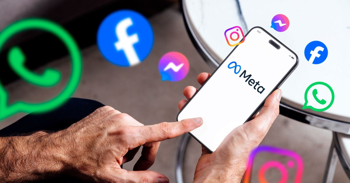 A imagem mostra uma mão segurando um smartphone que exibe o logotipo da Meta em destaque, com o texto “Meta” e o símbolo característico da empresa. Ao redor do dispositivo, há ícones flutuantes representando os principais aplicativos do ecossistema Meta: WhatsApp (ícones verdes com balão de conversa) Facebook (ícones azuis com a letra “f”) Instagram (ícones coloridos em tons de rosa, roxo e laranja) Messenger (ícones azuis com balão de mensagem) O fundo é neutro, com uma mesa metálica parcialmente visível, sugerindo um ambiente casual ou corporativo. A composição transmite a ideia de conectividade e integração entre as plataformas da Meta, reforçando sua presença no universo digital. redes sociais
