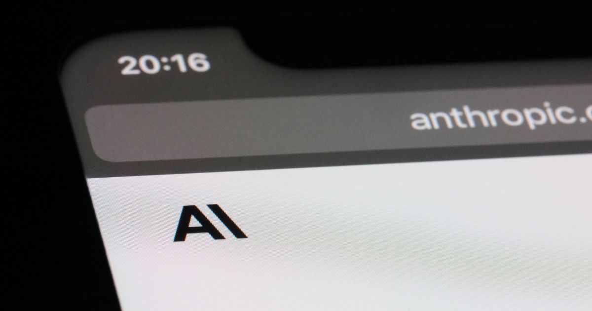A foto mostra um close-up da tela de um dispositivo móvel exibindo parte do site anthropic.com. No canto superior esquerdo aparece o horário 20:16, e no centro da tela está o texto “AI” em letras pretas sobre fundo branco. A imagem sugere um contexto relacionado à tecnologia e inteligência artificial.