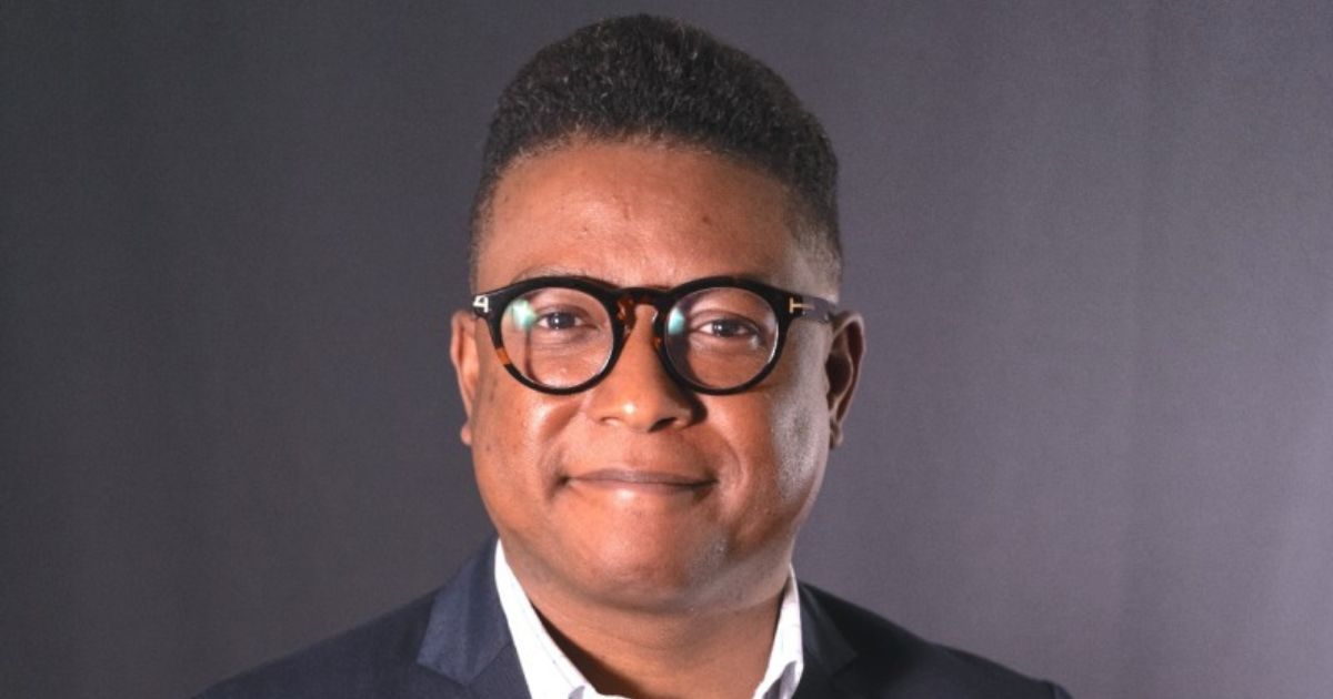 A imagem mostra uma pessoa vestindo traje formal, com uma camisa clara e um blazer escuro, em frente a um fundo neutro, sugerindo um cenário corporativo ou profissional. (Coca-Cola)